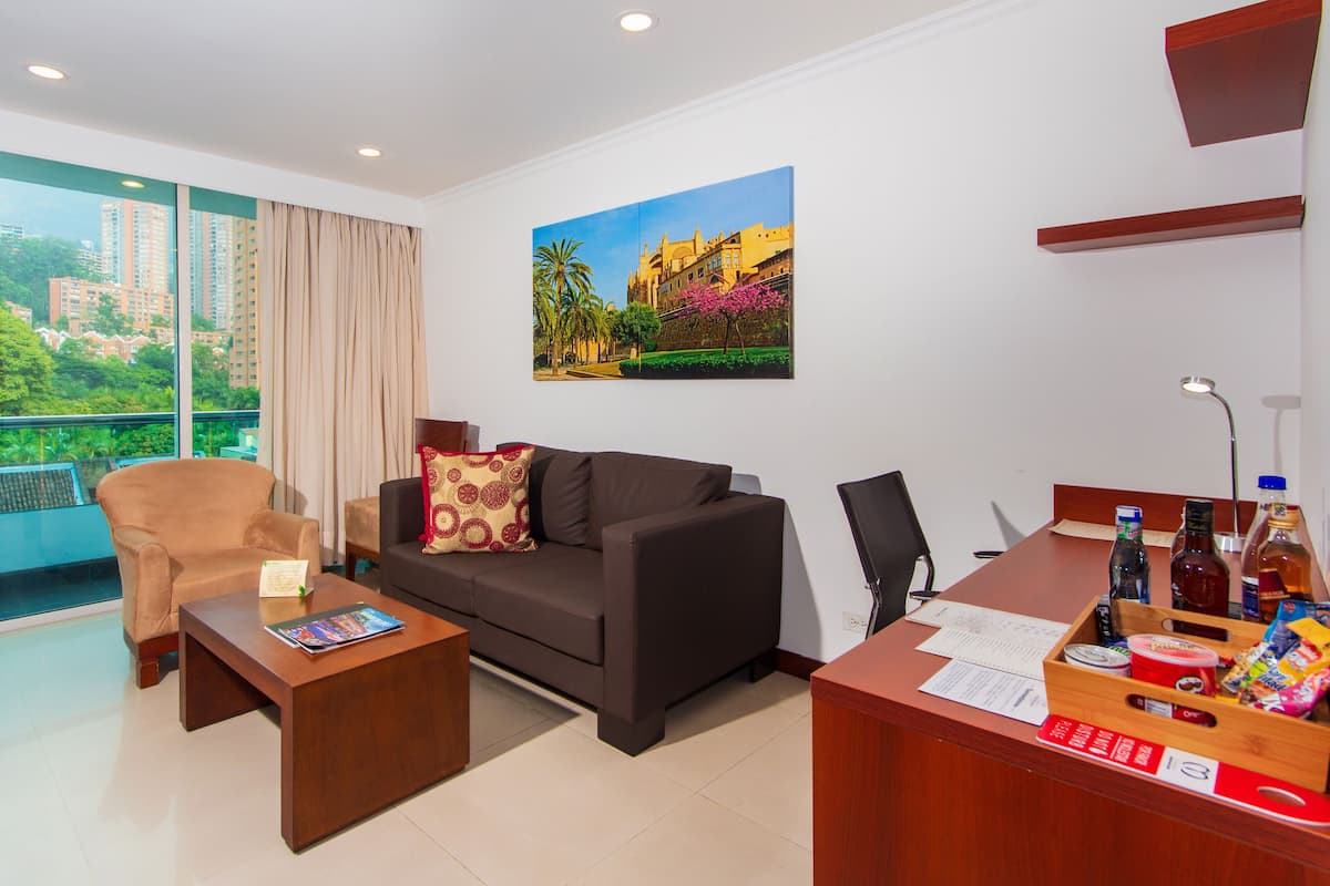 A modern living room with a sofa, armchair, coffee table, and a desk with various items.