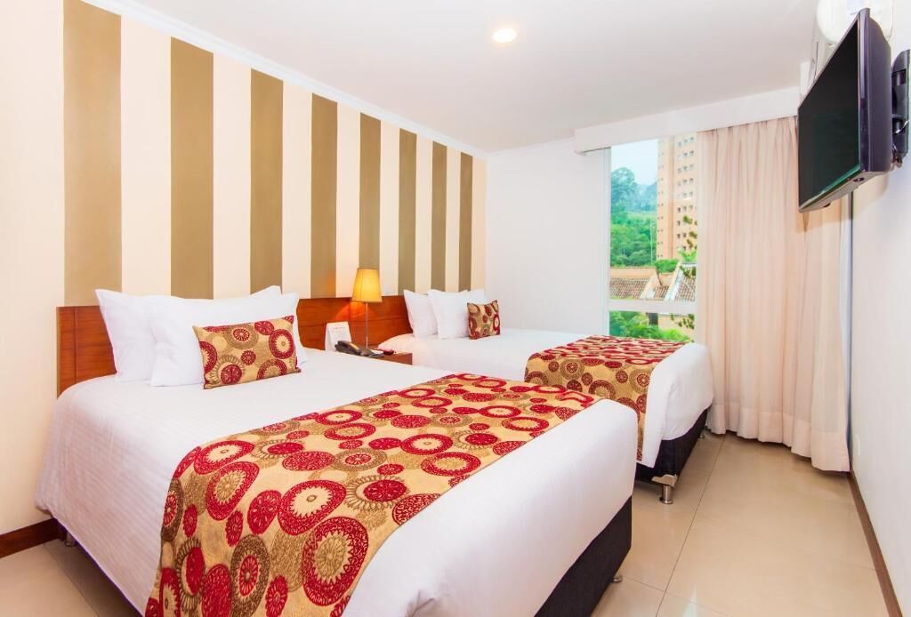 Una habitación de hotel con dos camas, un televisor montado en la pared y una ventana con cortinas.