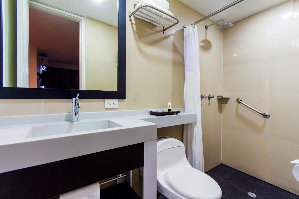 A modern bathroom with a white sink, mirror, and toilet. There is a towel rack above the sink and a shower curtain.