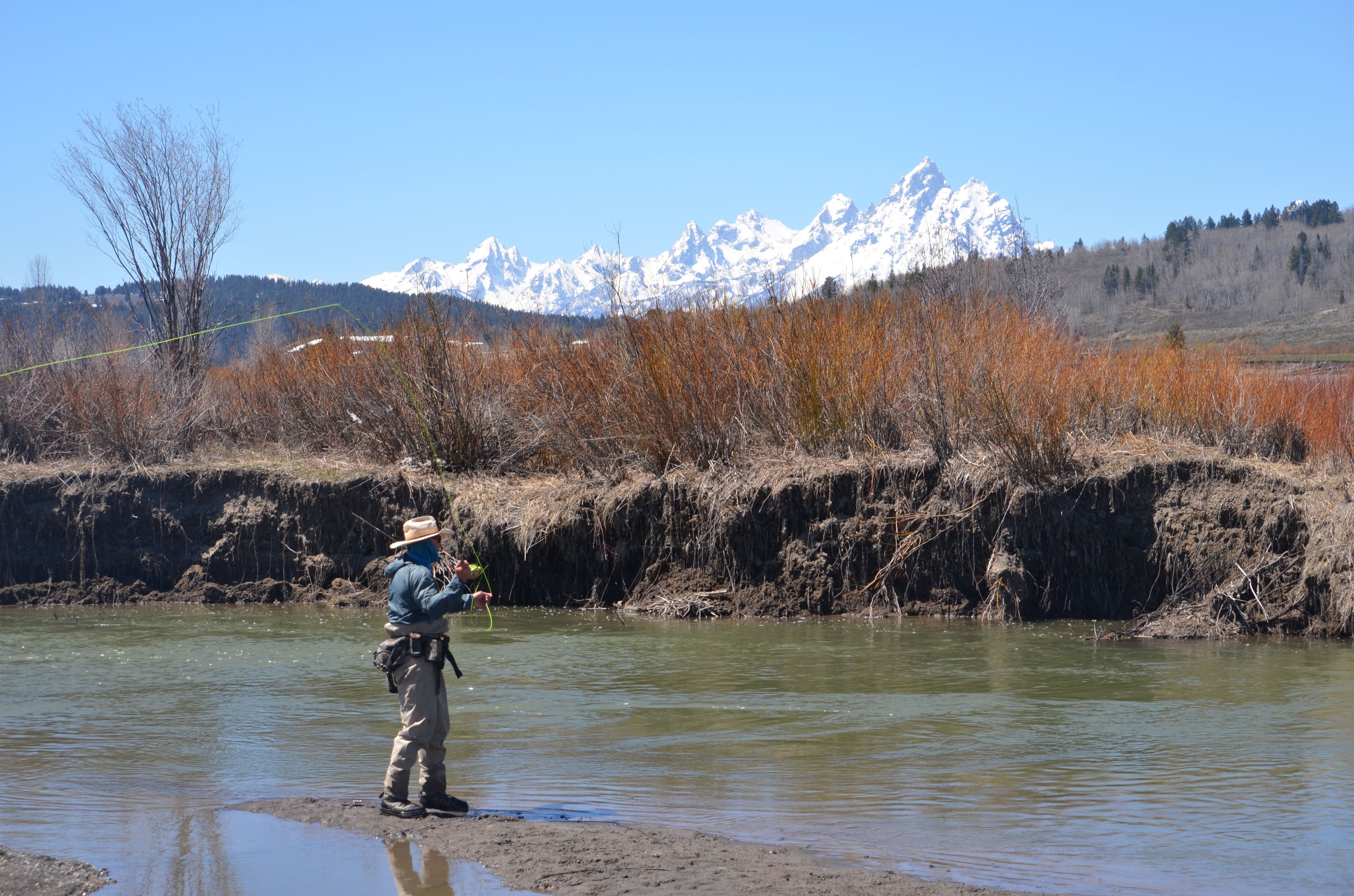 A person fishing by a river with a mountainous backdrop.