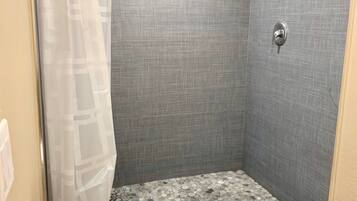 Un petit espace douche fermé, avec un mur gris texturé, un rideau de douche et un sol composé de petites pierres multicolores.
