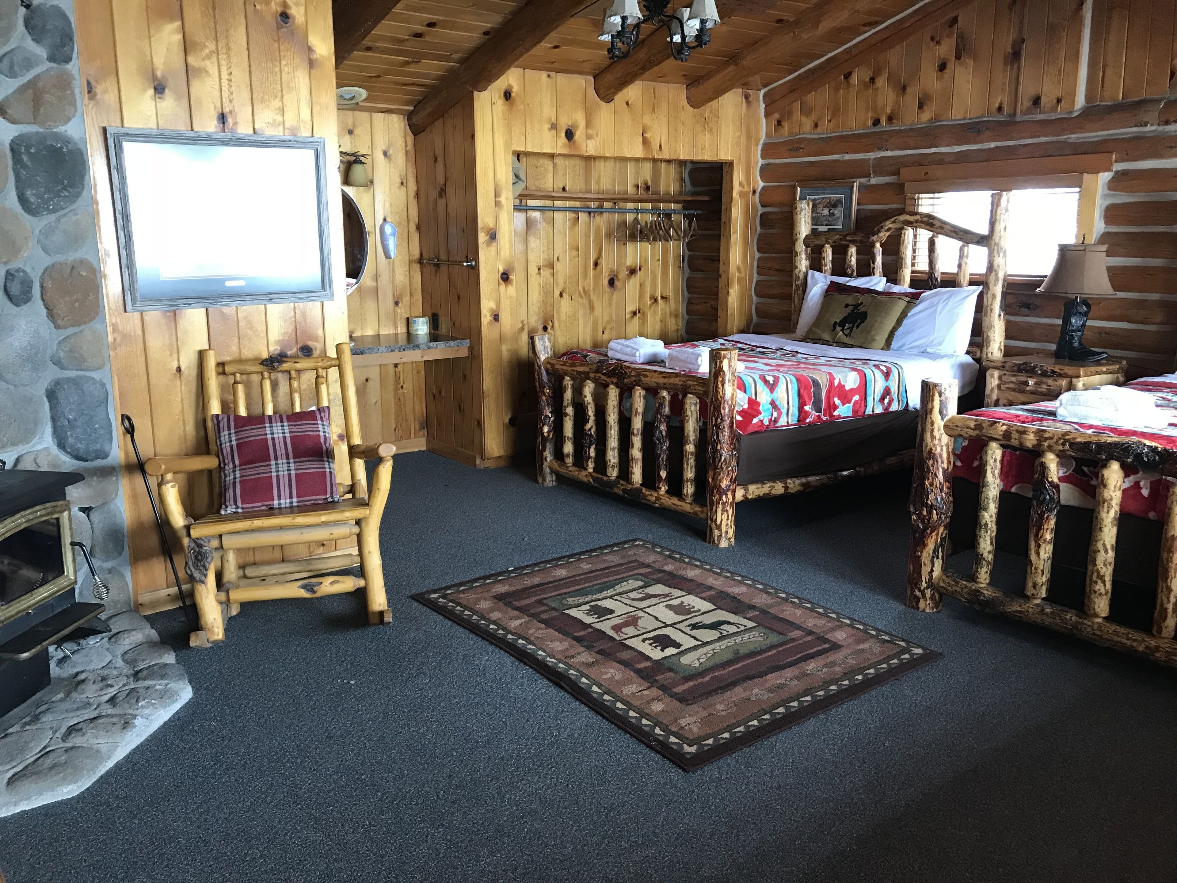 A log cabin room with a bed, a chair, a small table, a fireplace, and a television.