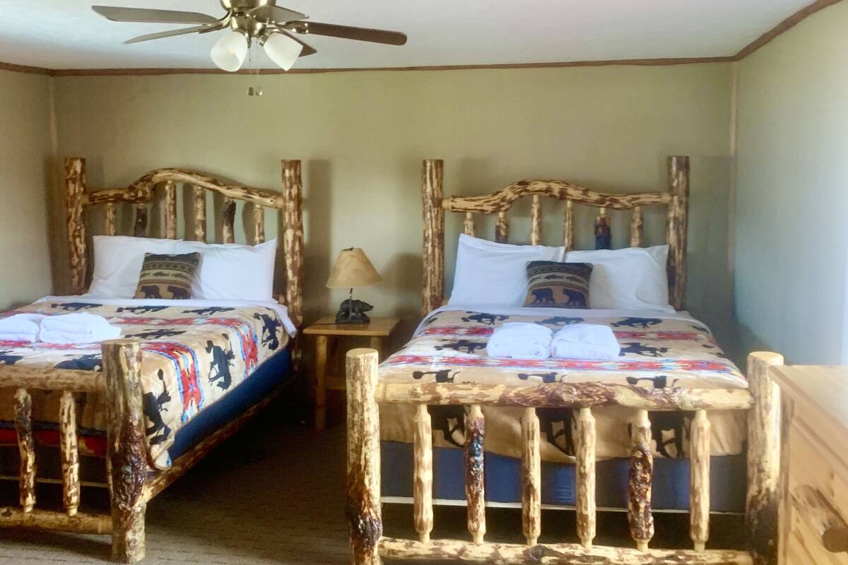 Una habitación con dos camas de madera, un ventilador de techo y una alfombra estampada.