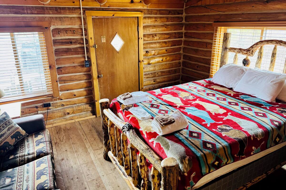 Una habitación tipo cabaña de madera con una cama de madera, un banco y una puerta.