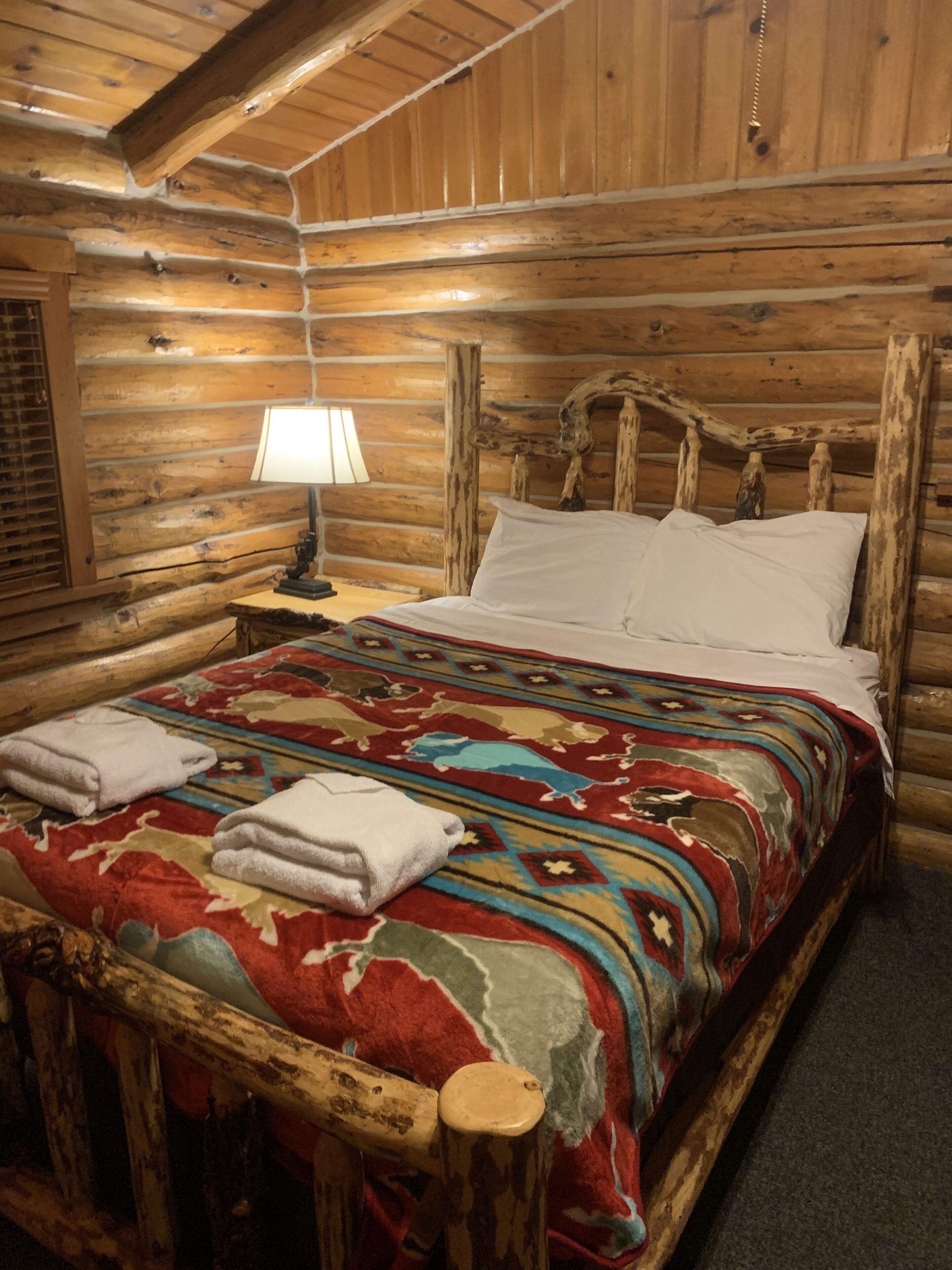 A log cabin bedroom with a wooden bed, a patterned blanket, and a bedside lamp.