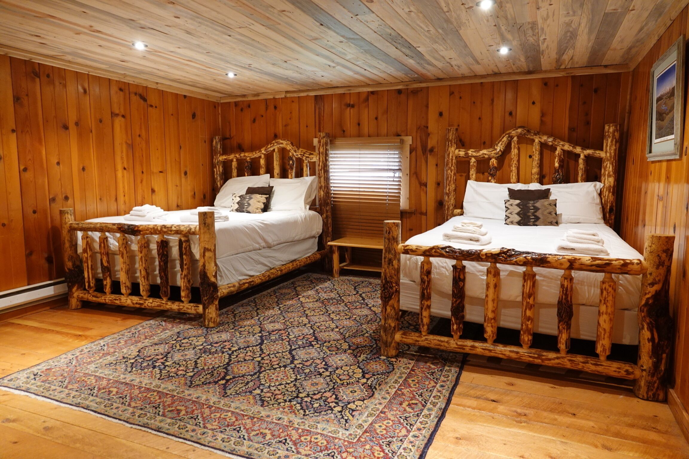 Una habitación de cabaña de madera con dos camas de madera, un tapete estampado y una ventana con persianas.