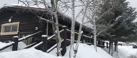 Una cabana de fusta amb un balcó de fusta i una finestra, envoltada d'arbres coberts de neu.