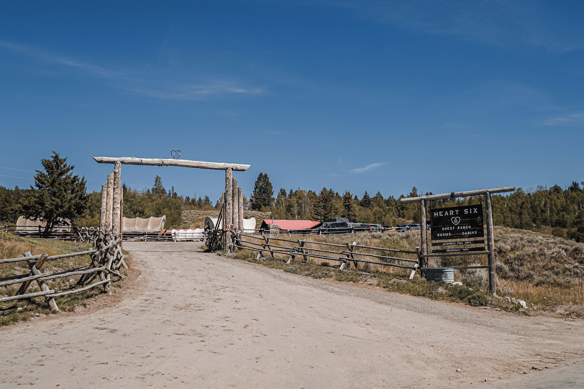 Una rústica puerta de madera con un letrero que anuncia Heart Six Guest Ranch, indicando habitaciones y cabañas.