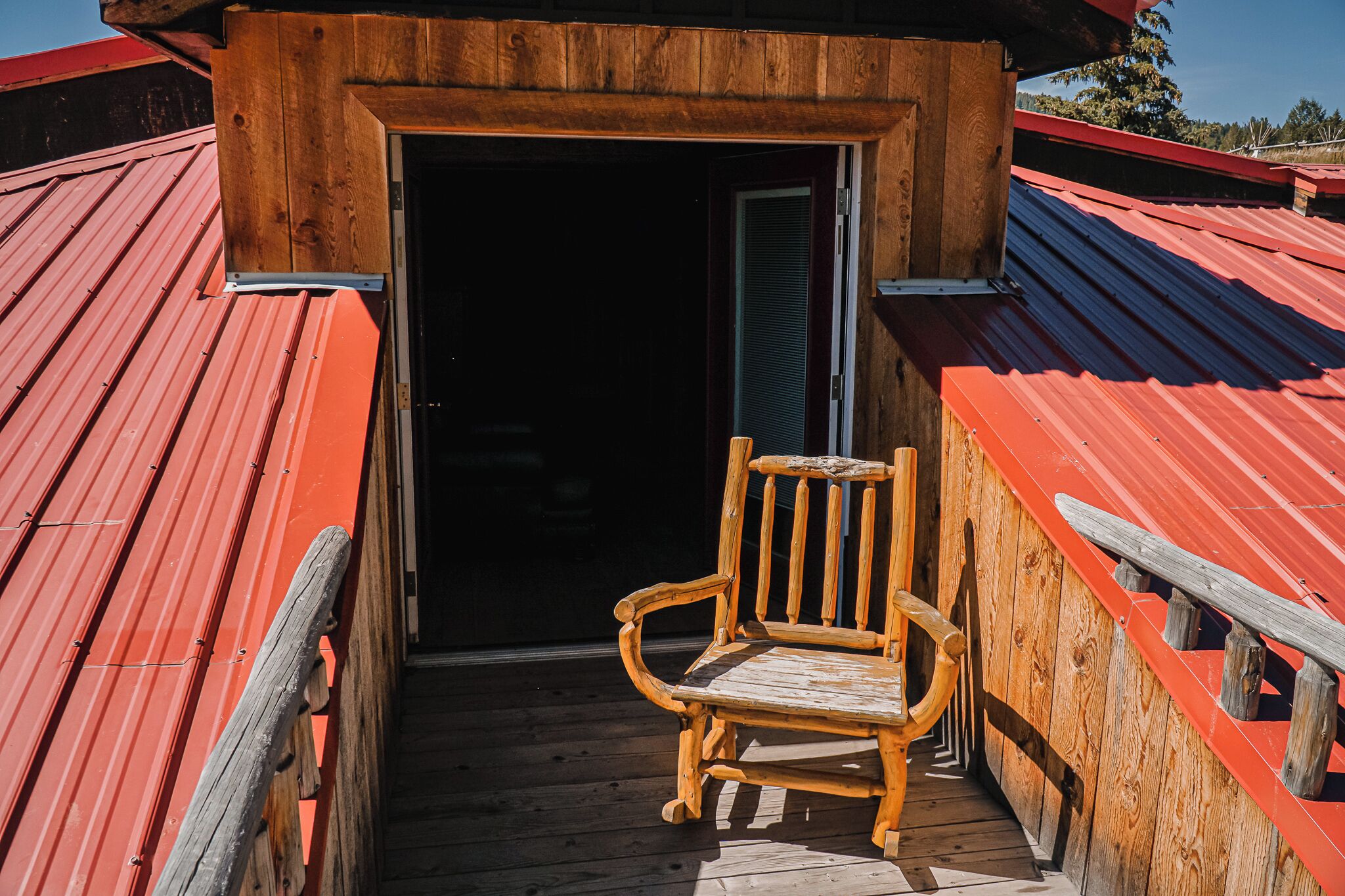 A wooden chair on a wooden deck with a red metal roof.