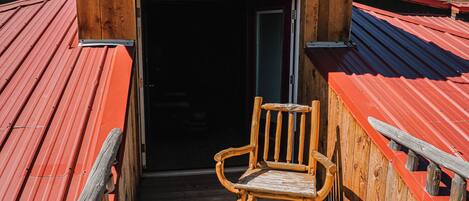A wooden chair on a wooden deck with a red metal roof.