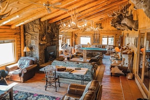 A log cabin interior with a stone fireplace, wooden ceiling beams, a pool table, and antler decorations. - Heart 6 Ranch (Moran)