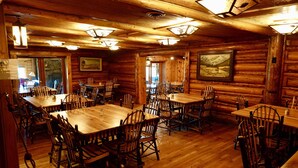 Un comedor de estilo cabaña de troncos con varias mesas y sillas de madera, paredes de madera y luces de techo.