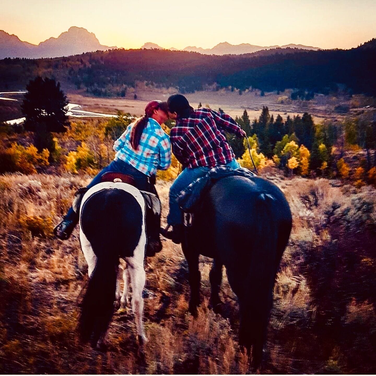 Two people riding a horse on a grassy hill with a mountain in the background.