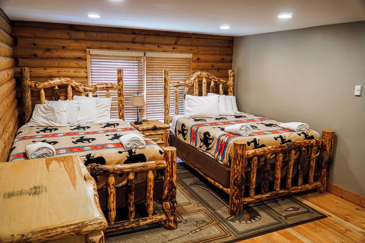 Un dormitorio de estilo cabaña de troncos con dos camas de madera, una mesa de madera y una ventana con persianas.