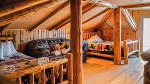 Una habitación acogedora tipo cabaña de madera con cama en altillo y sofá, vigas de madera y un estilo rústico.