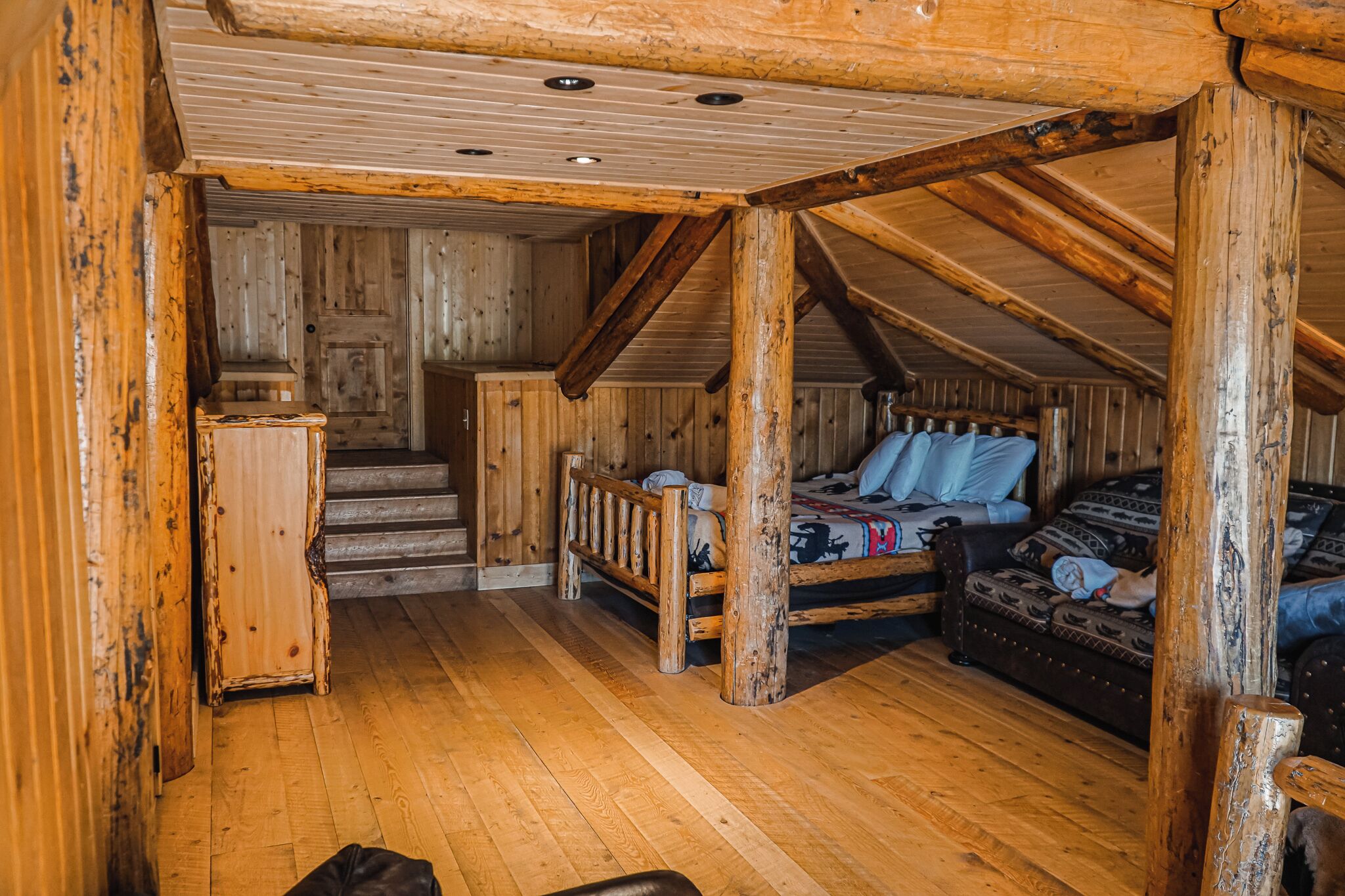 Un interior rústico de madera con cama estilo altillo, una mesita y una escalera que lleva a un nivel superior.