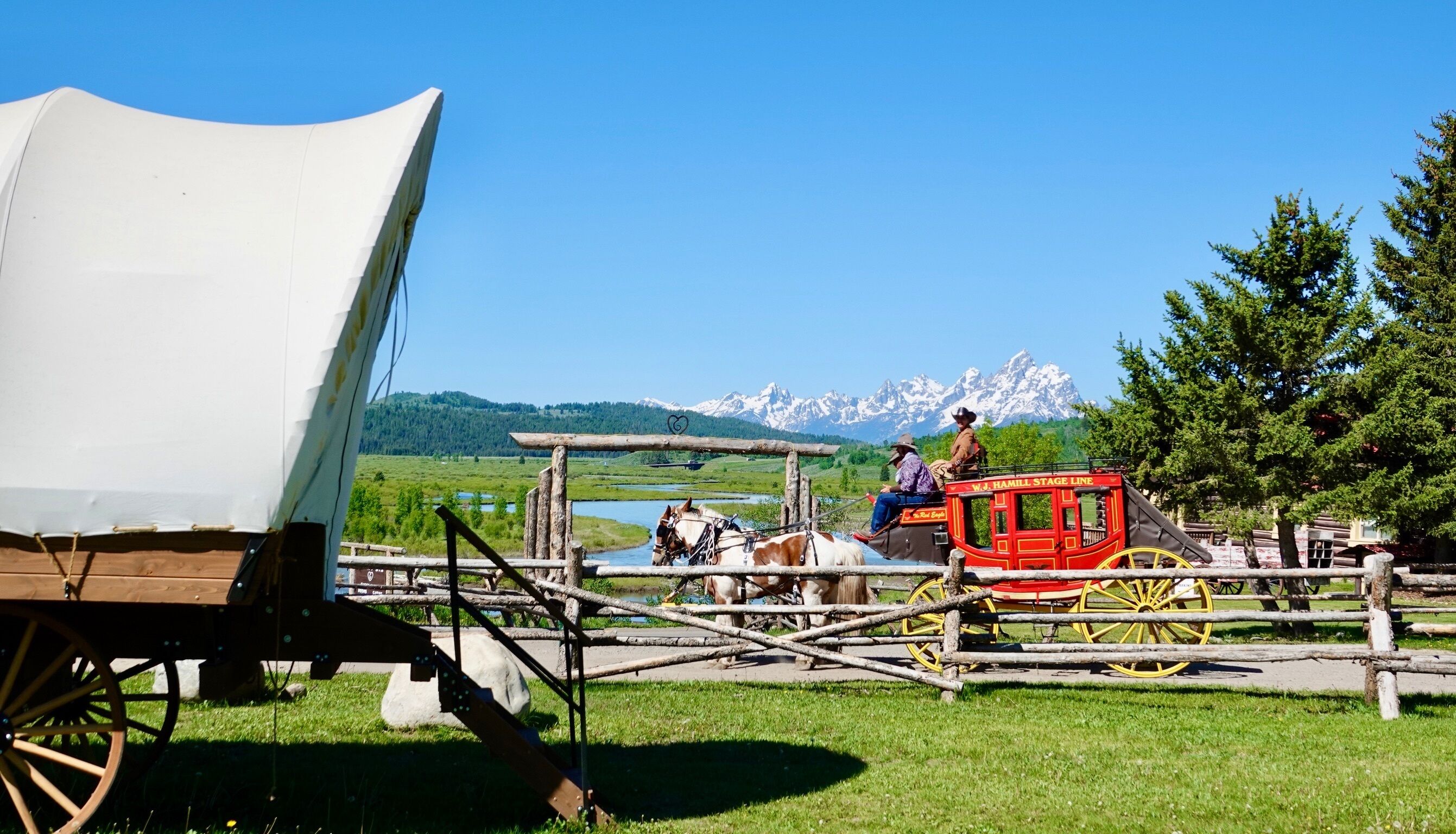 A stagecoach with passengers and horses, set against a backdrop of mountains and a clear sky.