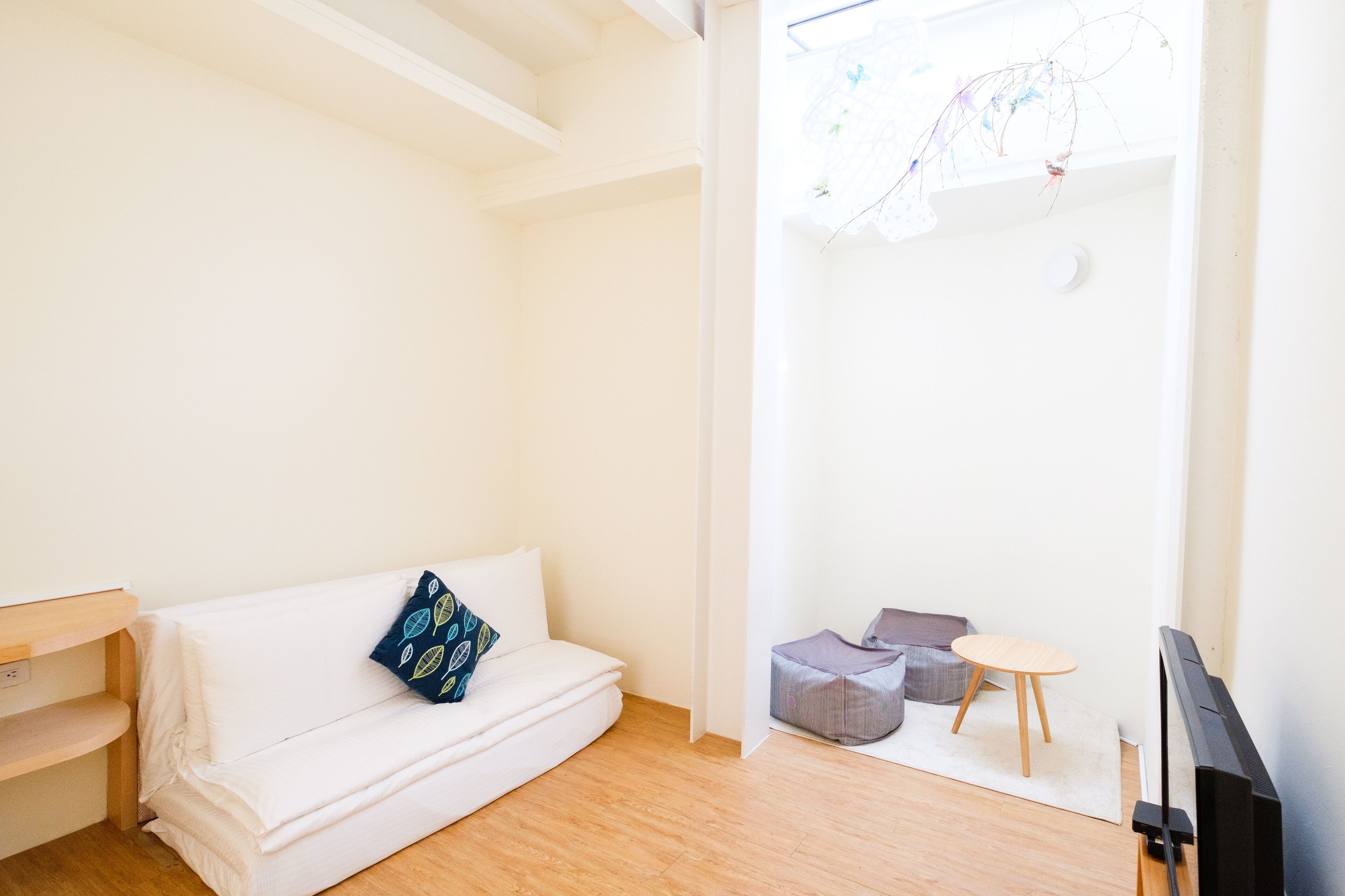 A bright, minimalistic room with a white sofa, a small round table, and a television.
