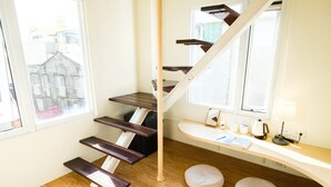 Uma escada moderna com degraus de madeira e corrimão branco, que leva a um patamar com uma mesa e uma janela.