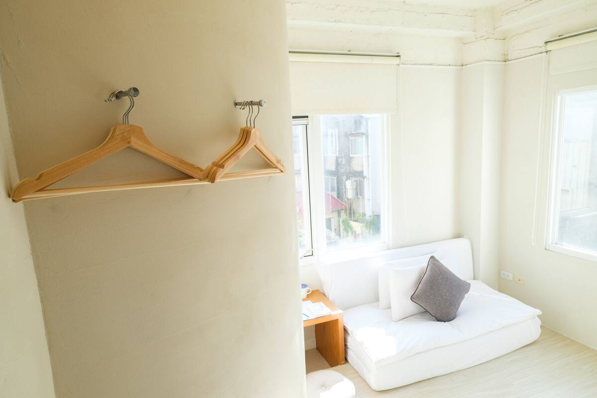 A bright room with a white sofa, wooden hangers on a wall, and a window with a view of buildings.