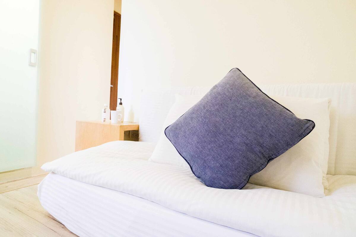 A neatly made bed with white bedding and a single dark-colored pillow.