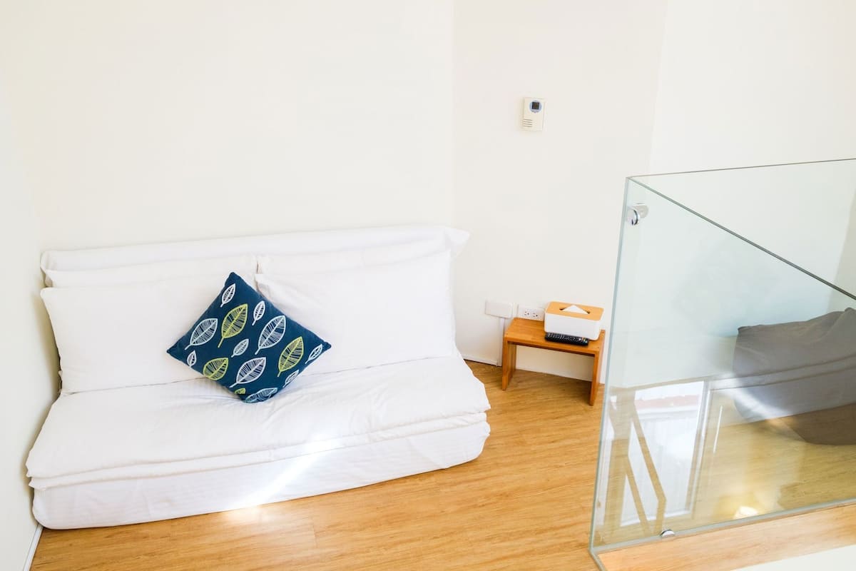 A white sofa with a blue pillow, a small wooden side table with a tissue box, and a glass partition.