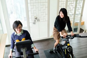 Two people using stationary bikes in a room with large windows and a geometric patterned door. - SSS Life Hotel (Tainan)