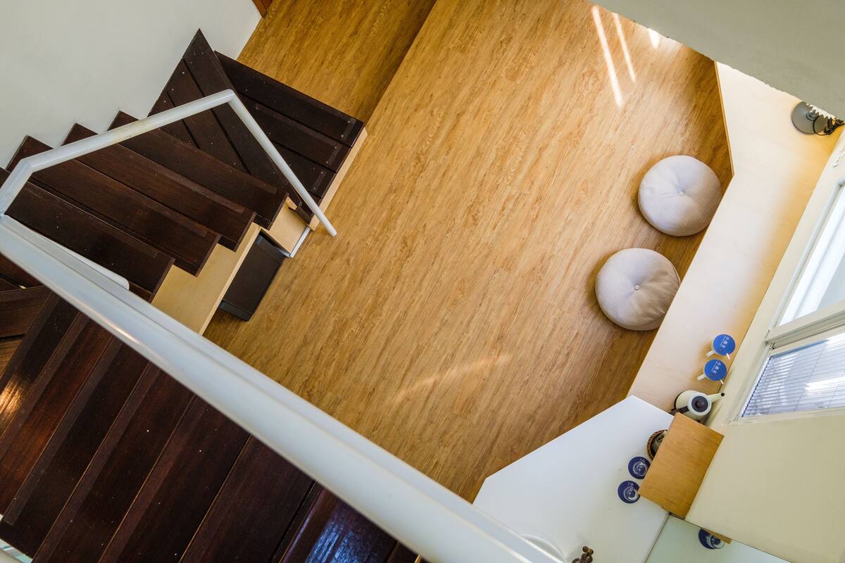 A modern interior with a wooden floor, a staircase, and a seating area with cushions.