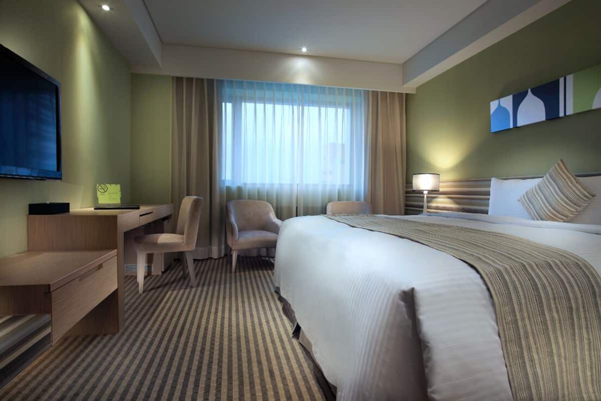 A hotel room with a bed, a desk, a chair, a TV, and a window with curtains.