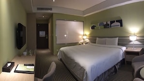A hotel room with a large bed, two bedside tables with lamps, a chair, and a desk with a tissue box and remote control. - Park City Central (Taichung)