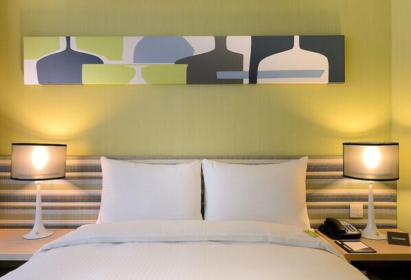 Una habitación de hotel con una cama, dos lámparas de noche, un teléfono y un cartel de bienvenida.