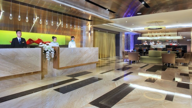 A hotel lobby with a marble reception desk, seating area, and a modern kitchen in the background. - Park City Central (Taichung)