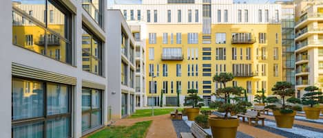 A courtyard with a yellow building, outdoor seating, and potted plants.