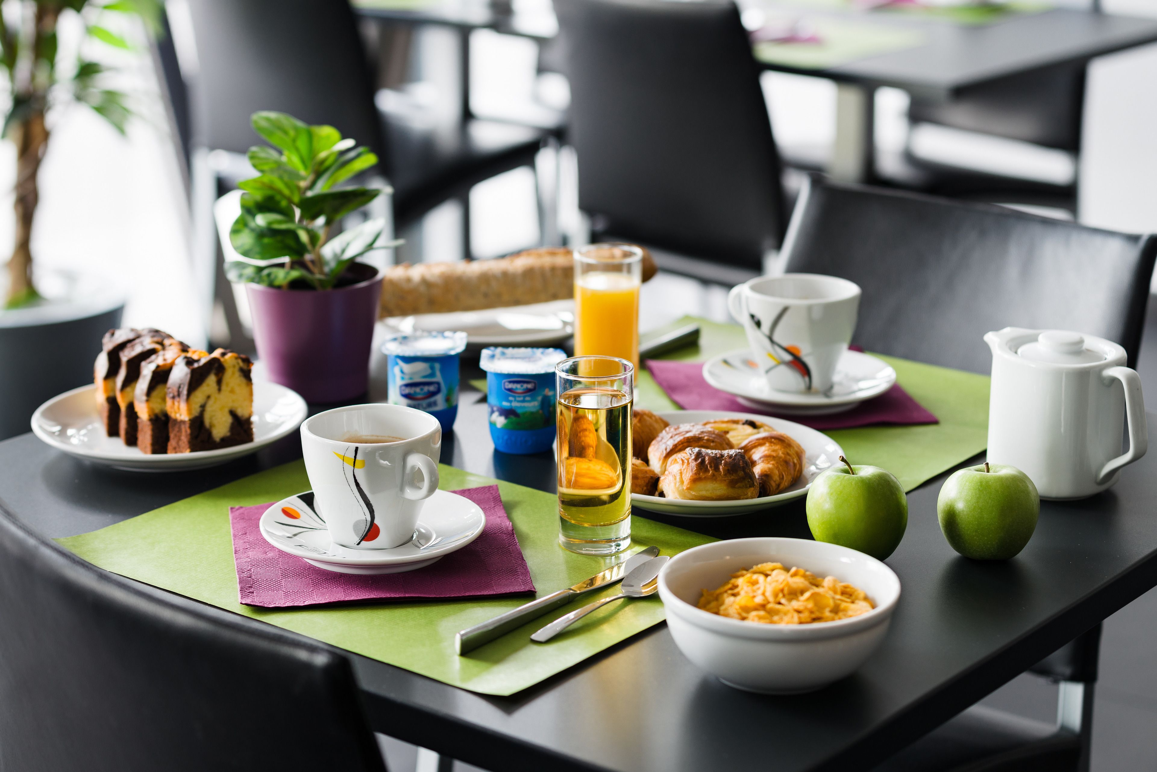 A breakfast table with a variety of food items, including a croissant, a slice of cake, and a bowl of cereal.