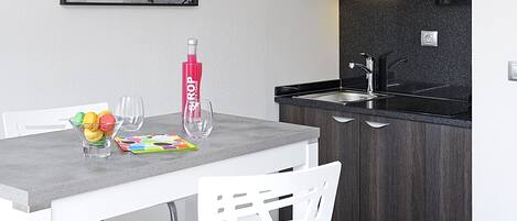 A modern kitchen with dark wood cabinets, a grey countertop, and a white dining table with a glass of water and a bottle of water.