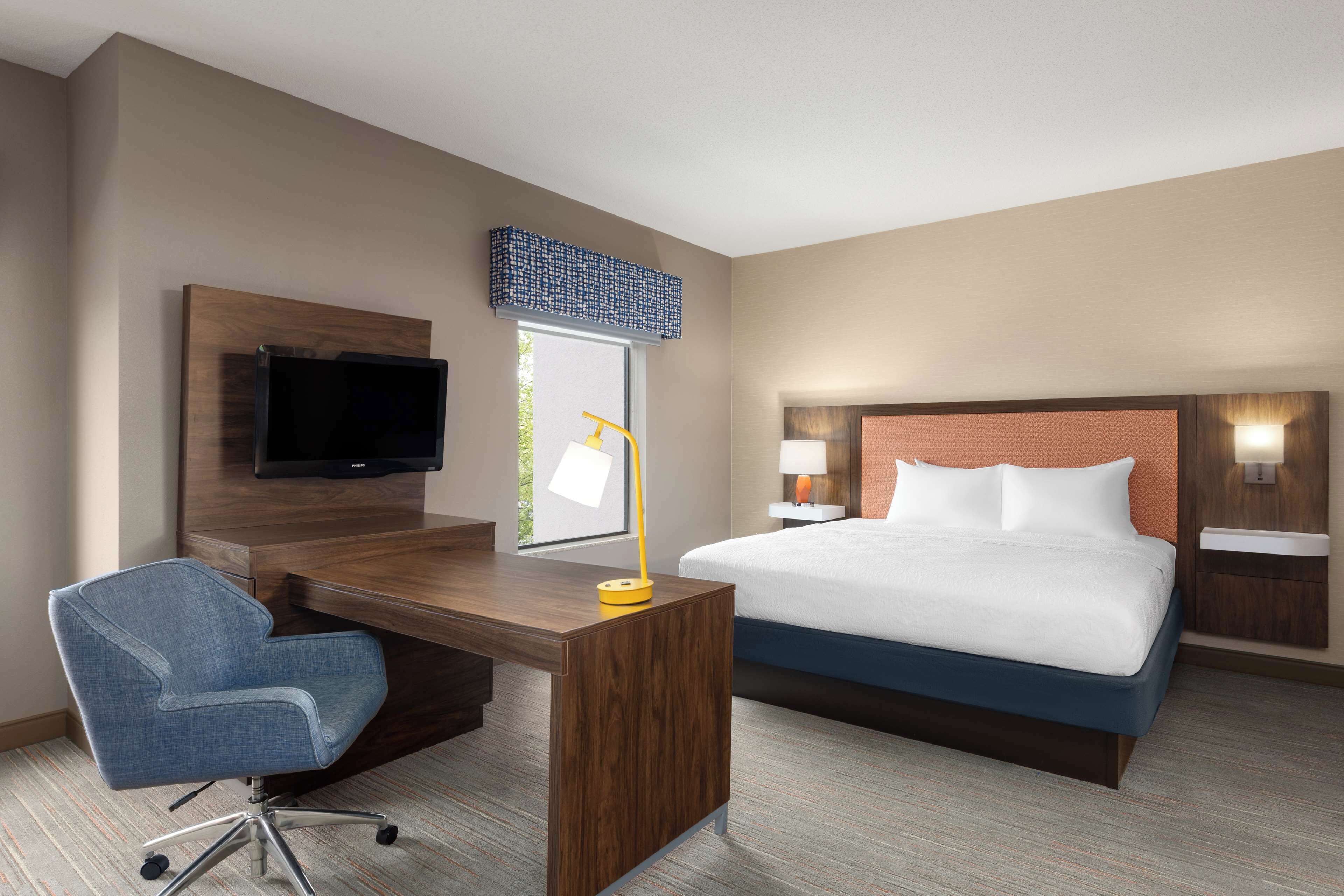 A hotel room with a bed, a desk with a chair, a television, and a window with a view.