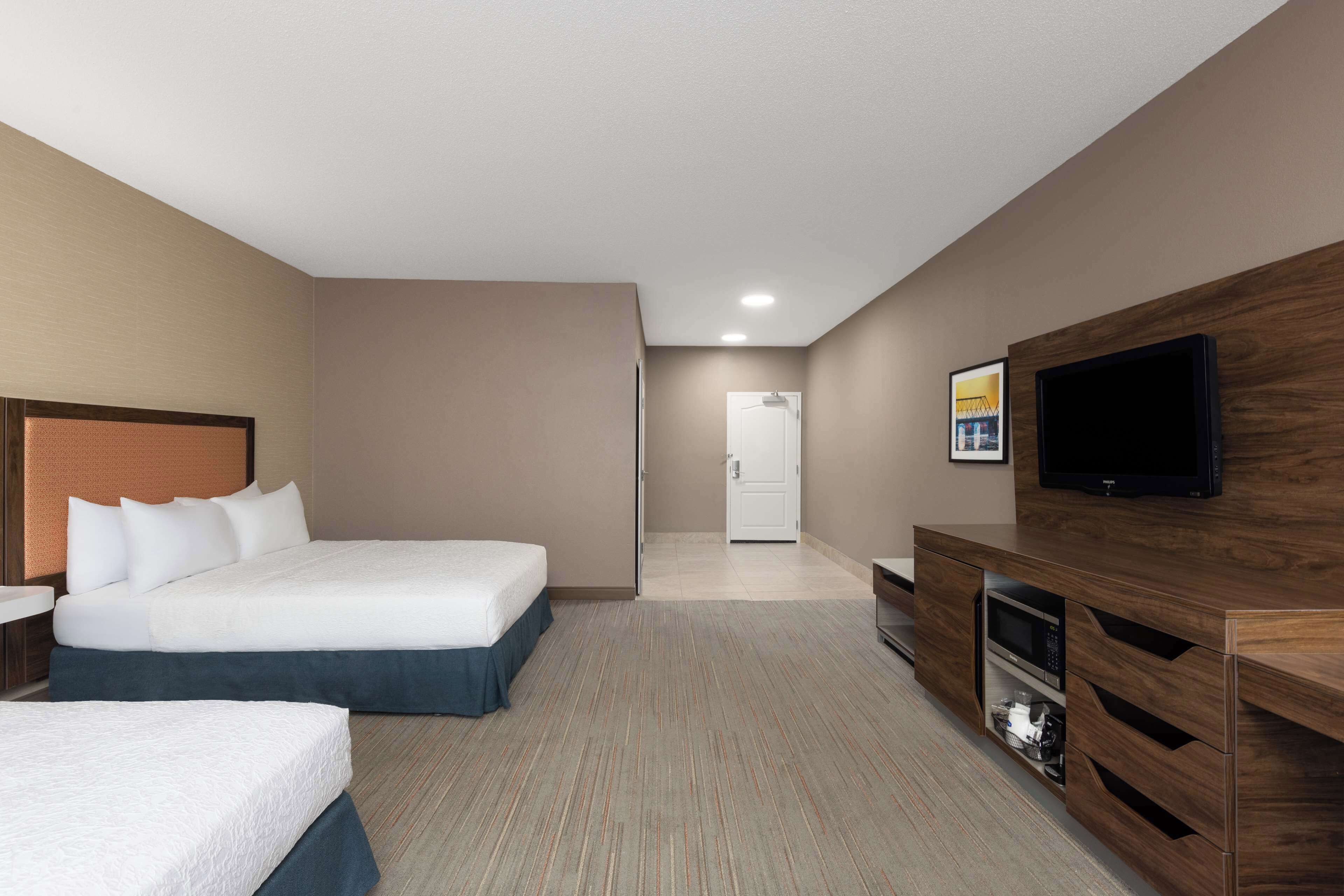 Ein Hotelzimmer mit einem großen Bett, einem Fernseher, einem Holzkasten und einer Tür zu einem anderen Raum.