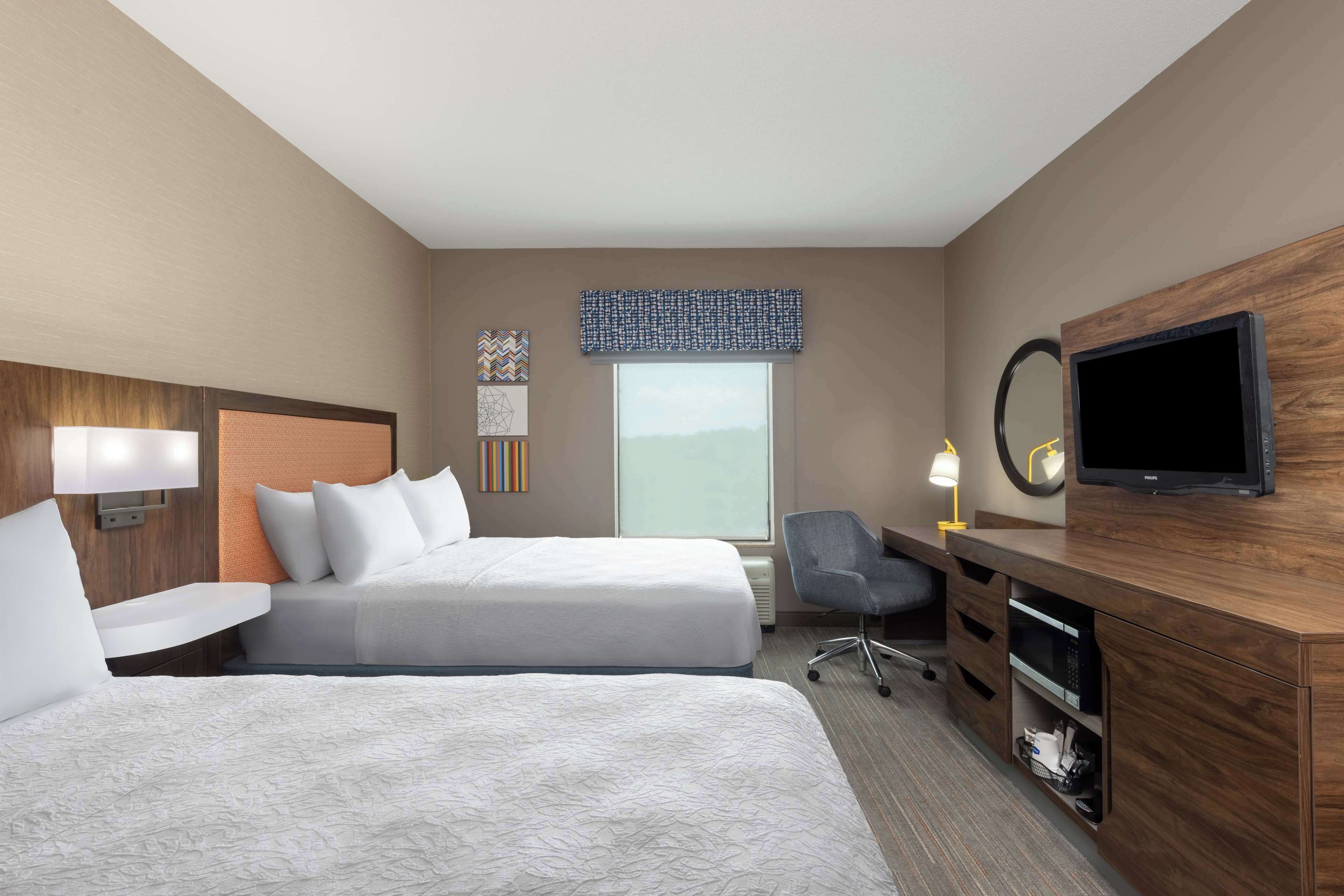 Une chambre d’hôtel avec deux lits, un bureau, une chaise, une télévision et une grande fenêtre.