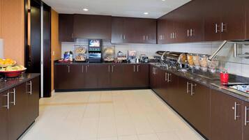 A modern kitchen with dark wooden cabinets, a stainless steel sink, and a breakfast bar with various food items.