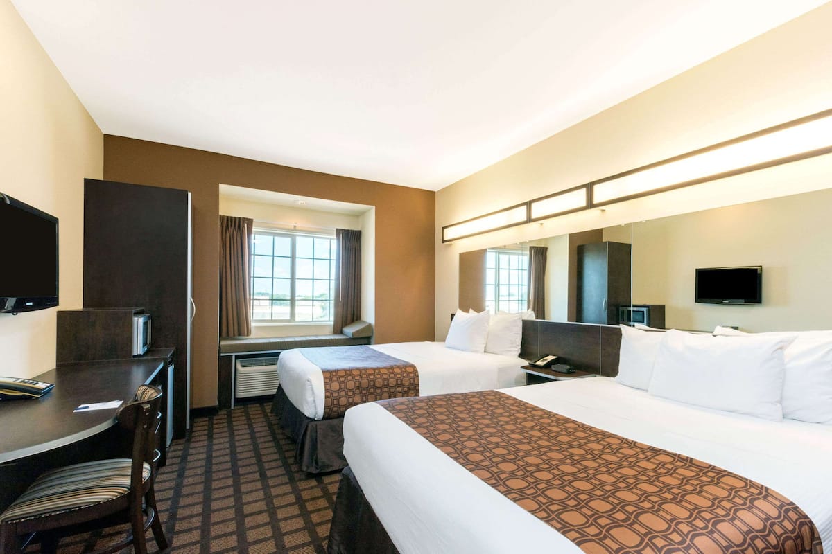Una habitación de hotel con dos camas, un escritorio con silla, un televisor y una ventana con cortinas.