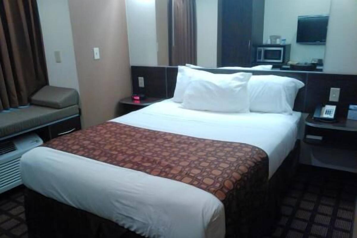 A hotel room with a bed, a bedside table with a phone, a TV, and a sofa.