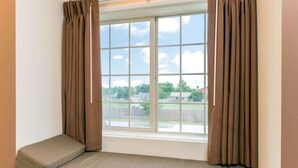 A room with a window, brown curtains, a bench, and a view of a residential area. - Microtel Inn and Suites Eagle Pass (Eagle Pass)