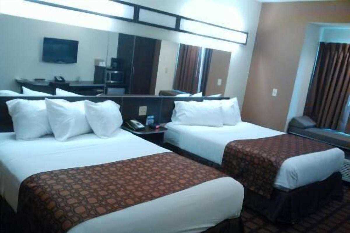 A hotel room with two beds, a desk, a chair, a television, and a mirror.