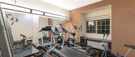 Un gimnasio con cinta de correr, elíptica y banco de pesas.