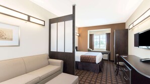 A hotel room with a sofa, a bed with a patterned bedspread, a desk with a chair, a television, and a window with curtains. - Microtel Inn and Suites Eagle Pass (Eagle Pass)