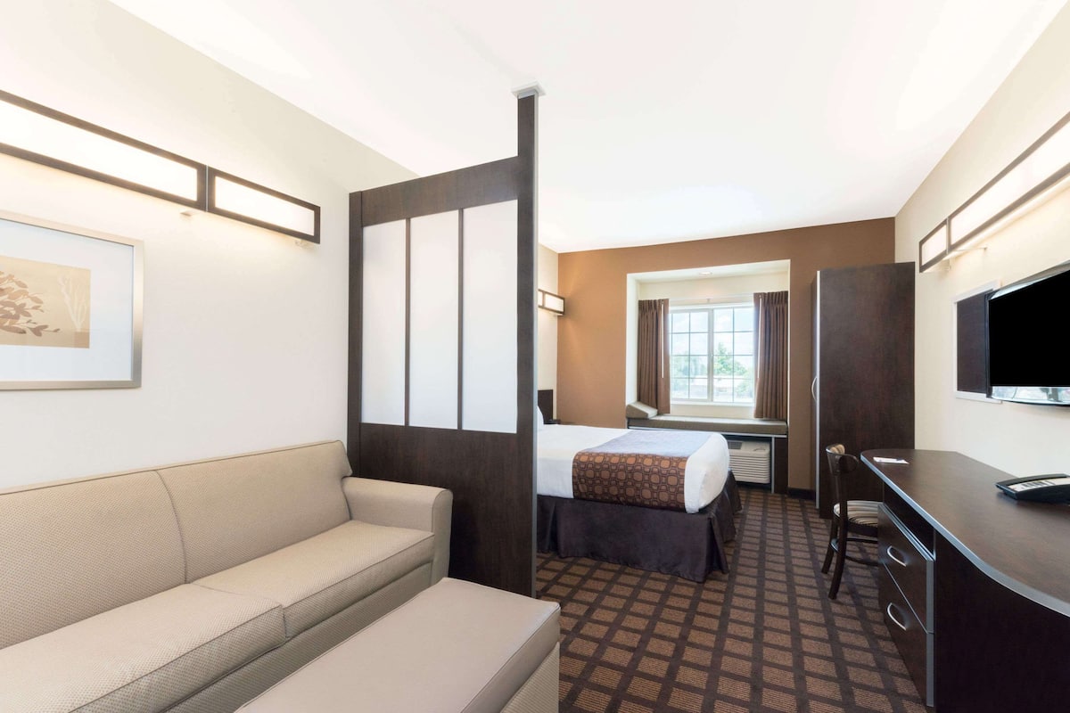 Una habitación de hotel con sofá, cama con colcha estampada, escritorio con silla, televisor y ventana con cortinas.