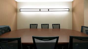 Un salón de conferencias con una larga mesa y seis sillas, una lámpara fijada a la pared y paredes lisas.