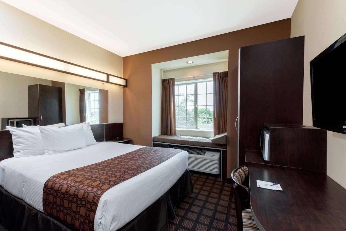 Habitación de hotel con una cama grande, un escritorio, una silla, un televisor de pantalla plana y una ventana con cortinas.