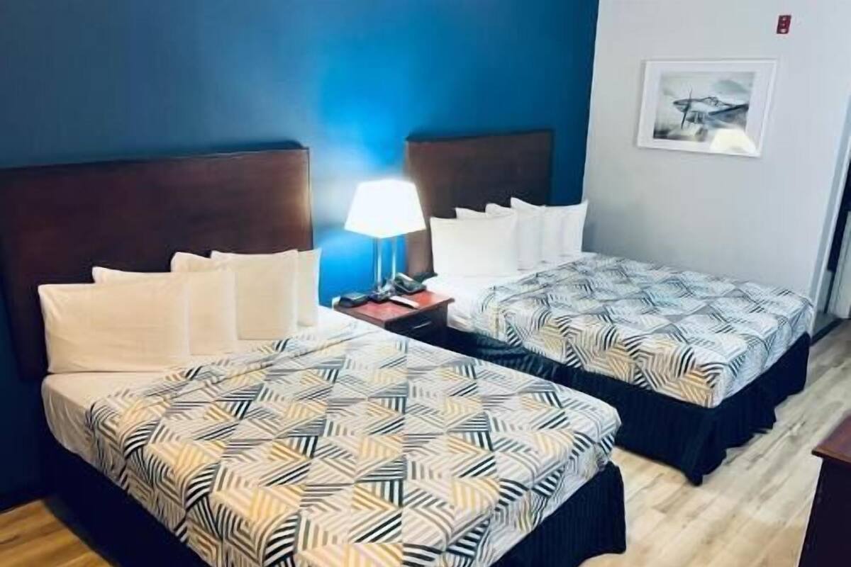 A hotel room with two beds, a nightstand with a lamp, a framed picture on the wall, and a wooden floor.