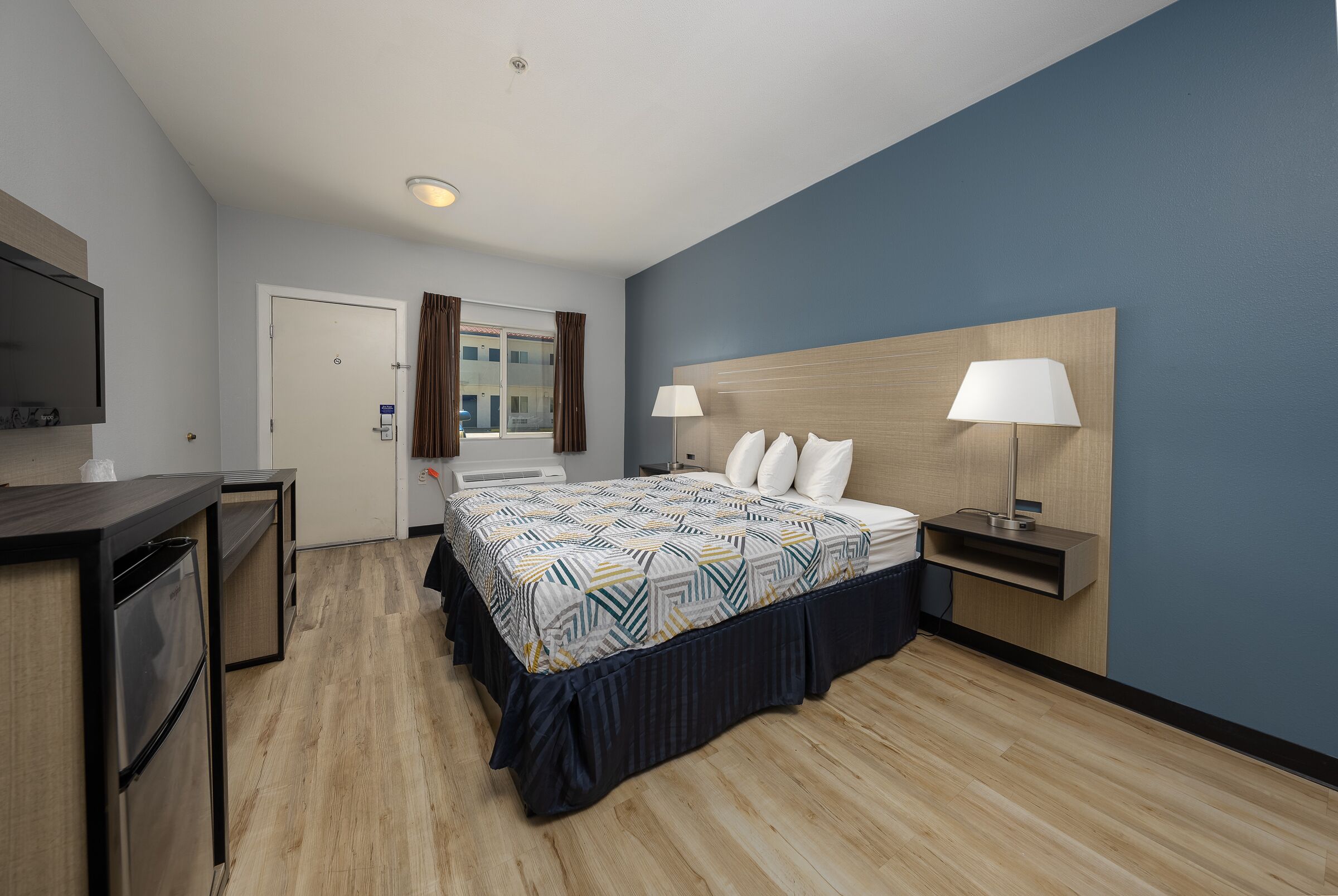 Habitación de hotel con cama, mesitas de noche, televisión, escritorio y ventana con cortinas.
